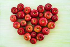 Ein Herz aus reifen roten Äpfeln auf grünem Holzhintergrund, Draufsicht. foto