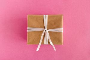 geschenkbox aus bastelpapier und weißem band auf dem rosa hintergrund, draufsicht. foto