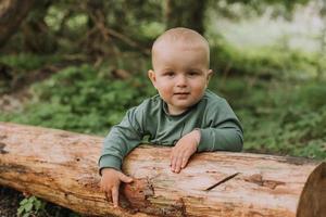 Porträt eines süßen kleinen Jungen, der sich vor dem Hintergrund eines grünen Waldes an einem Baumstamm festhält. Kürbiskorb für Süßigkeiten im Vordergrund. Wandern und Spielen im Freien. Halloween-Konzept. hochwertiges Foto