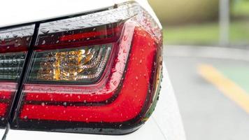 hinterlicht des weißen autos mit wassertropfenregen. auf der straße mit verschwommenen grünen blättern auf dem parkplatz. foto