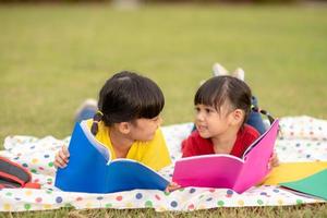 Kleines Mädchen und Schwester, die zusammen ein Buch im Park lesen. Entzückende asiatische Kinder, die es genießen, gemeinsam im Freien zu lernen. Bildung, Intelligenzkonzept foto