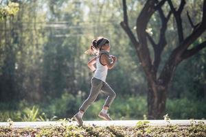 glückliches Kindermädchen, das im Sommer in der Natur im Park läuft. warmes sonnenlicht. asiatisches kleines läuft in einem park. Outdoor-Sport und Fitness, Übungs- und Wettbewerbslernen für die Entwicklung von Kindern. foto