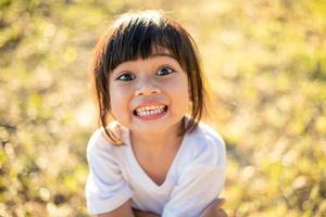 glückliches kleines asiatisches mädchenkind, das vordere zähne mit breitem lächeln zeigt und gesundes glückliches lustiges lächelndes gesicht lacht junges entzückendes reizendes weibliches kind. freudiges porträt des asiatischen grundschülers. foto