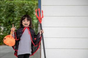 asiatisches Mädchen im Dämonenkostüm mit schwarzem und rotem Dreizack, fröhliches Halloween-Konzept foto