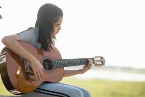 Schönes Mädchen, Gitarre spielen, singen, Musik oder Glückskonzept, warmer Lichttoneffekt bei Sonnenuntergang. foto