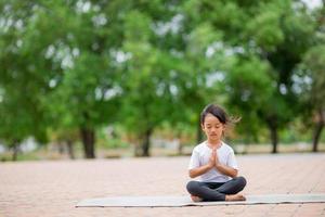 kleines süßes asiatisches mädchen, das yoga-pose auf einer matte im park praktiziert, gesundes und übungskonzept foto