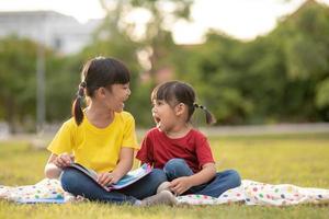 Zwei schöne kleine Mädchen, die Bücher im Garten lesen, sitzen auf Gras. das konzept von bildung und freundschaft. foto