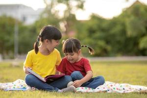 Zwei schöne kleine Mädchen, die Bücher im Garten lesen, sitzen auf Gras. das konzept von bildung und freundschaft. foto