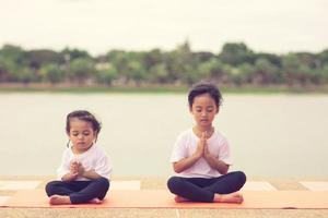 kleines süßes asiatisches mädchen, das yoga-pose auf einer matte im park praktiziert, gesundes und übungskonzept foto