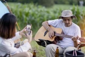 Glückliches asiatisches Paar spielt Gitarre und singt, genießt Camping und trinkt Bier. foto