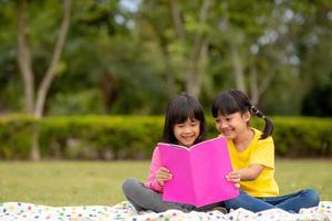 Zwei schöne kleine Mädchen, die Bücher im Garten lesen, sitzen auf Gras. das konzept von bildung und freundschaft. foto