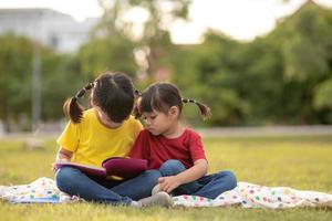 Zwei schöne kleine Mädchen, die Bücher im Garten lesen, sitzen auf Gras. das konzept von bildung und freundschaft. foto