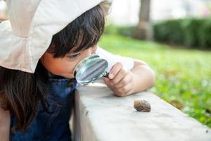 Fröhliches Mädchen, das die Natur mit einer Lupe und einer Schnecke erkundet. er hat Spaß im Garten. das konzept des kindes ist bereit, zur schule zu gehen. foto