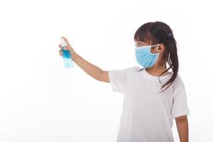 Süßes asiatisches Mädchen, das eine Maske trägt und sich die Hände mit Alkohol wäscht, um die Ausbreitung der Krankheit auf weißem Hintergrund zu verhindern. prävention der ausbreitung des influenzavirus koronare covid-19 influenza foto