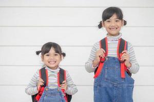 zurück zur Schule. Zwei süße asiatische Mädchen mit Schultaschen, die ein Buch auf weißem Hintergrund zusammenhalten foto