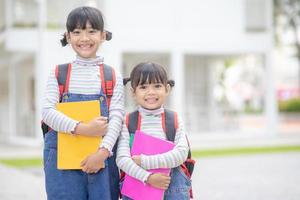 zurück zur Schule. Zwei süße asiatische Mädchen mit Schultasche, die ein Buch in der Schule zusammenhalten foto