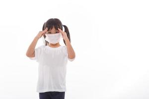 Asiatisches Kind, das eine medizinische Maske trägt, verspürt Kopfschmerzen auf weißem Hintergrund. foto