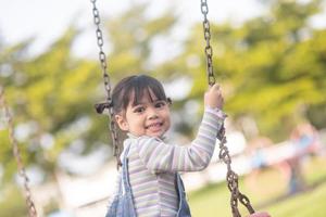 glückliches kleines asiatisches Mädchen, das Schaukel im Freien im Park spielt foto