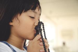 Kleines asiatisches Mädchen, das mit dem Halten des Kreuzes betet, christliches Konzept. foto