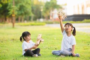 Zwei kleine Kinder spielen tagsüber mit einem Spielzeugflugzeug aus Pappe im Park. Konzept des glücklichen Spiels. Kind hat Spaß im Freien. foto