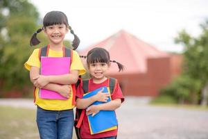 zurück zur Schule. Zwei süße asiatische Mädchen mit Schultasche, die ein Buch in der Schule zusammenhalten foto