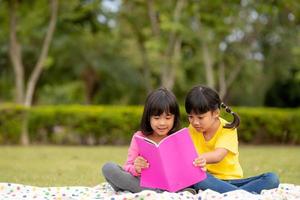 Zwei schöne kleine Mädchen, die Bücher im Garten lesen, sitzen auf Gras. das konzept von bildung und freundschaft. foto