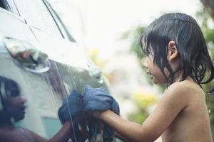 süßes asiatisches Kind, das am Sommertag ein Auto mit Schlauch wäscht foto