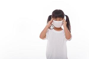 Asiatisches Kind, das eine medizinische Maske trägt, verspürt Kopfschmerzen auf weißem Hintergrund. foto