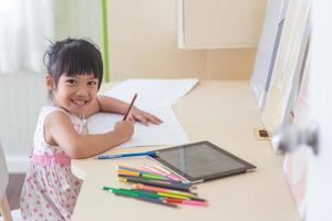 kleines asiatisches kind, das mit einem bleistift auf notizbuch am schreibtisch schreibt foto