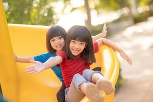 Süße kleine Mädchen Geschwister amüsieren sich an sonnigen Sommertagen auf dem Spielplatz im Freien. Kinder auf Plastikrutsche. lustige Aktivität für Kinder. aktive sportfreizeit für kinder foto