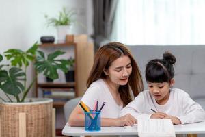 schöne asiatische frau, die ihrer tochter zu hause bei den hausaufgaben hilft. foto