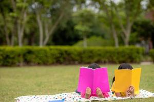 Zwei schöne kleine Mädchen, die Bücher im Garten lesen, sitzen auf Gras. das konzept von bildung und freundschaft. foto