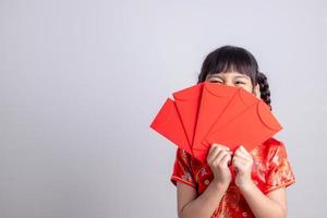 Fröhliches kleines asiatisches Mädchen in traditioneller chinesischer Kleidung, das lächelt und einen roten Umschlag hält. frohes chinesisches neujahrskonzept. foto