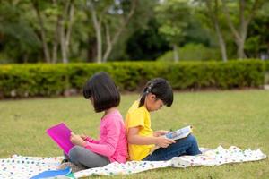 Zwei schöne kleine Mädchen, die Bücher im Garten lesen, sitzen auf Gras. das konzept von bildung und freundschaft. foto