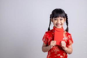 Fröhliches kleines asiatisches Mädchen in traditioneller chinesischer Kleidung, das lächelt und einen roten Umschlag hält. frohes chinesisches neujahrskonzept. foto