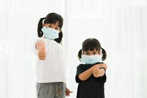 zwei kleine asiatische mädchen mit maske zum schutz pm2.5 und zeigen daumen hoch geste für gute luft im freien. luftverschmutzung pm2.5 und coronavirus-konzept foto