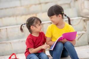 kleines Mädchen und Schwester, die zusammen ein Buch lesen. Entzückende asiatische Kinder, die es genießen, gemeinsam im Freien zu lernen. Bildung, Intelligenzkonzept foto