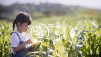 das kleine mädchen analysiert mit einem tablet das wachstum von pflanzen auf dem landwirtschaftlichen grundstück und visual icon., das landwirtschaftliche technologiekonzept. Smart-Farming-Lernkonzept foto