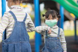 neuer normaler lebensstil, soziales distanzierungskonzept. glückliche kinder, die gesichtsmasken tragen und sich auf dem spielplatz amüsieren, schützen coronavirus covid-19, foto