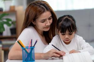 schöne asiatische frau, die ihrer tochter zu hause bei den hausaufgaben hilft. foto