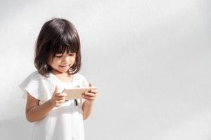 Ein kleines Mädchen konzentriert sich auf das Telefon, schaut auf das Smartphone, Technologiekonzept für Kinder, Profilansicht, isoliert auf weißem Hintergrund, Kopierraum foto