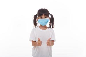 kleines asiatisches mädchen, das maske zum schutz von pm2.5 trägt und daumen hoch geste für gute luft im freien zeigt. luftverschmutzung pm2.5 und coronavirus-konzept foto