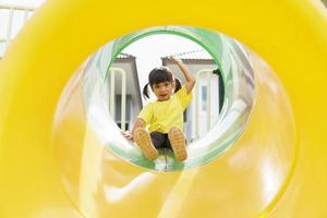 Kind spielt auf Spielplatz im Freien. kinder spielen auf dem hof der schule oder des kindergartens. aktives kind auf bunter rutsche und schaukel. gesunde sommeraktivität für kinder. foto