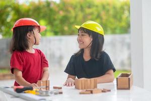 asiatische geschwistermädchen, die technikhüte tragen, bauen häuser aus dem holzspielzeug. um zu lernen und die Entwicklung zu verbessern, kleiner Architekt. foto