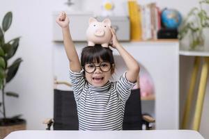 kleines asiatisches mädchen, das geld in einem sparschwein spart, über sparen lernt, kind spart geld für zukünftige bildung. geld, finanzen, versicherungen und personenkonzept foto