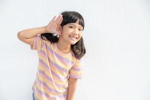 Kleines asiatisches Mädchen hält ihre Hand in der Nähe ihres Ohrs und hört zu. Tag der Behinderung. taubes Kind. aufregendes Gesicht auf asiatischem Kindermädchen. Schalten Sie das Telefon aus und hören Sie Ihrem Kind zu. foto