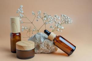 Braunglasflaschen mit Serum, Creme oder ätherischem Öl. beiger hintergrund mit stein und schönen blumen. Hautpflege Naturkosmetik. Schönheitskonzept für Gesichts- und Körperpflege foto