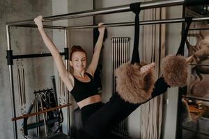 Fröhliche Sportlerin mit einem Lächeln, das sich auf Pilates-Reformer ausdehnt foto