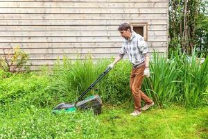 Mann schneidet grünes Gras mit Rasenmäher im Hinterhof. Gartenland-Lifestyle-Hintergrund. schöne aussicht auf frischen grünen rasen im sonnenlicht, gartenlandschaft im frühling oder in der sommersaison. foto