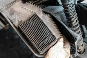 Mechaniker hält schmutzigen Luftfilter des Motorrads in der Garage. Schmutziger Luftfilter behindert den Luftstrom. wartung, reparatur motorradkonzept foto